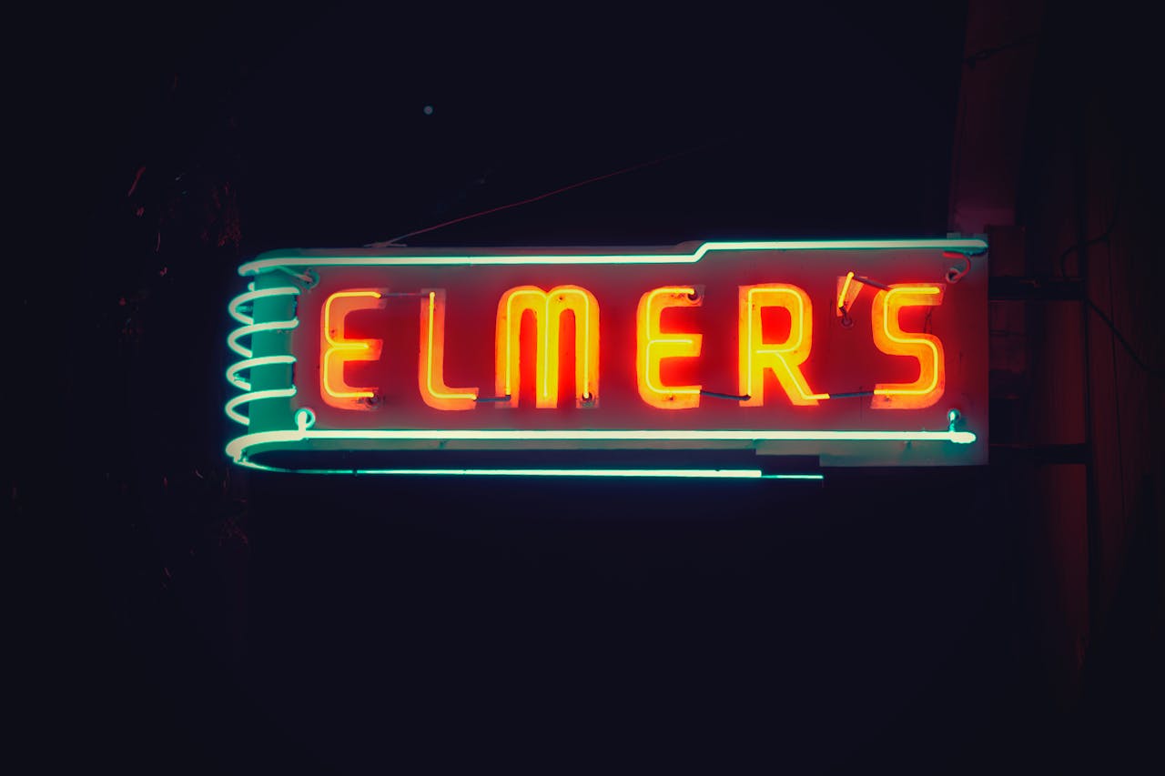 services-03 A glowing neon sign displaying 'Elmer's' in vibrant colors against a dark night sky.